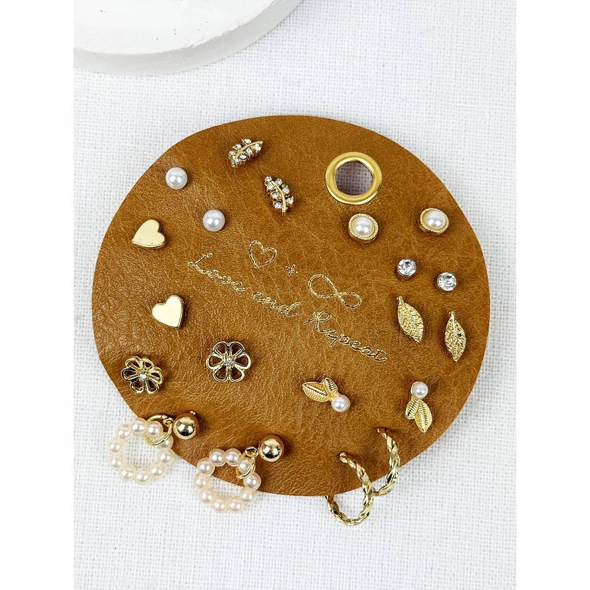 Round brown leather jewelry tray with various gold and pearl earrings on a white background