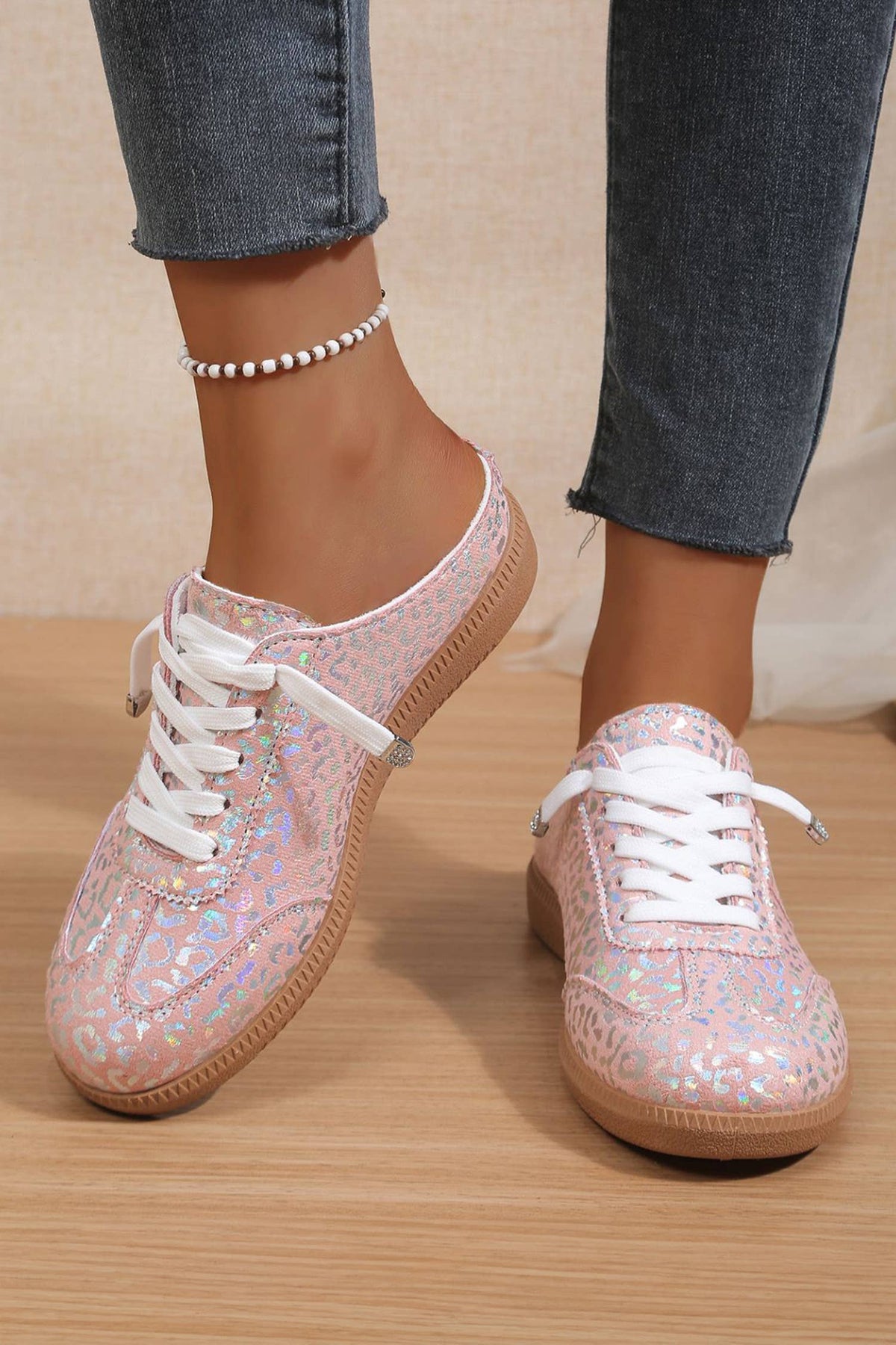 Woman trying on pink glittery leopard sneakers with white laces on a wooden floor.