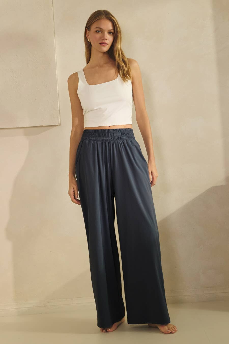 Woman wearing a white top and navy wide-leg pants against a neutral background