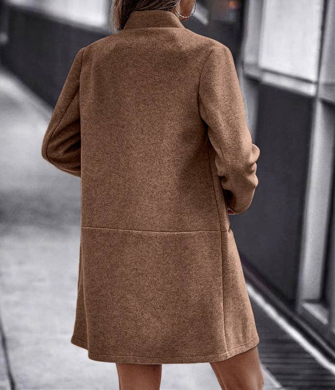 A woman viewed from behind wearing a mid-length brown coat in an outdoor urban setting.