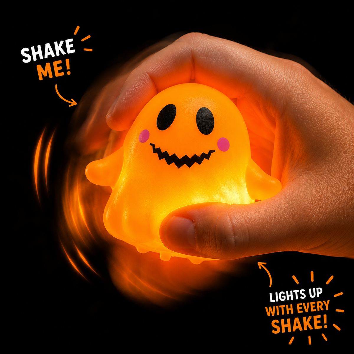 A hand holds a glowing orange ghost-shaped stress toy against a black background. The toy has a simple black face with pink cheeks and is surrounded by motion blur and text that says 'SHAKE ME!' and 'LIGHTS UP WITH EVERY SHAKE!'.