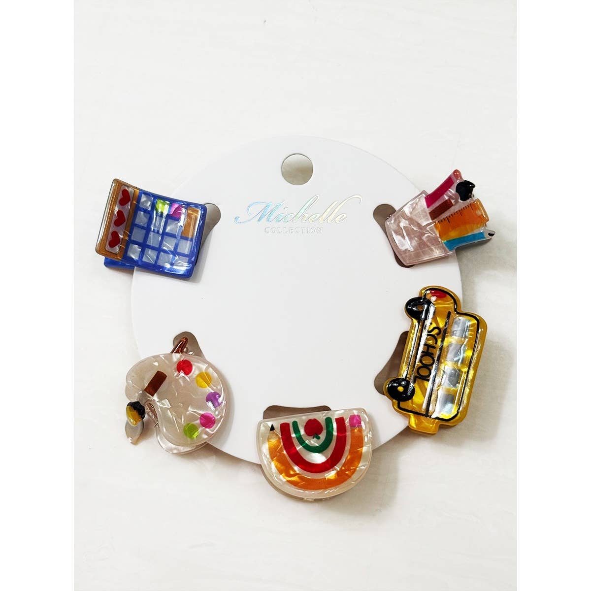 Set of colorful school themed hair clips including a school bus, rainbow, calculator, pencil holder, and paint palette on a white background.