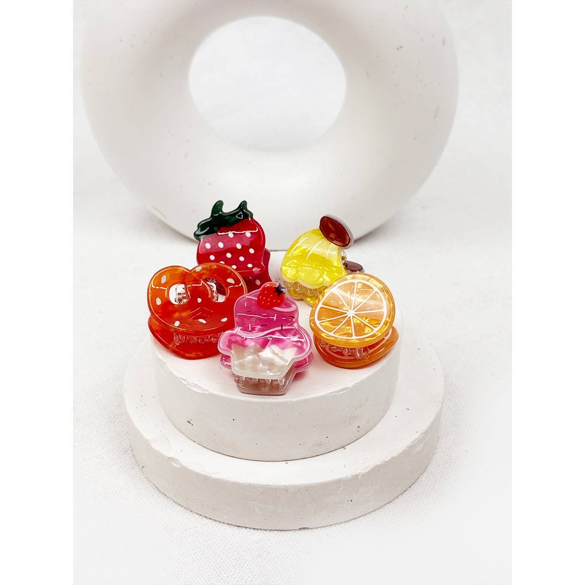 Colorful fruit-shaped hair clips on a white stand with a white background