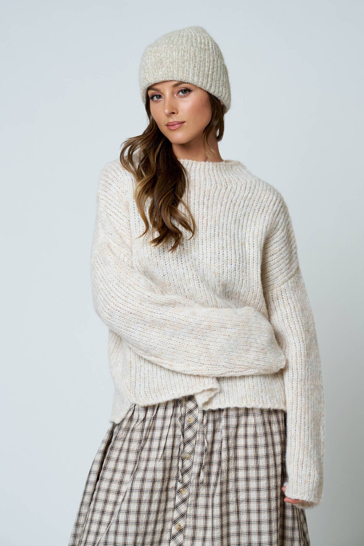 Woman wearing a cream knit sweater and beanie against a light gray background