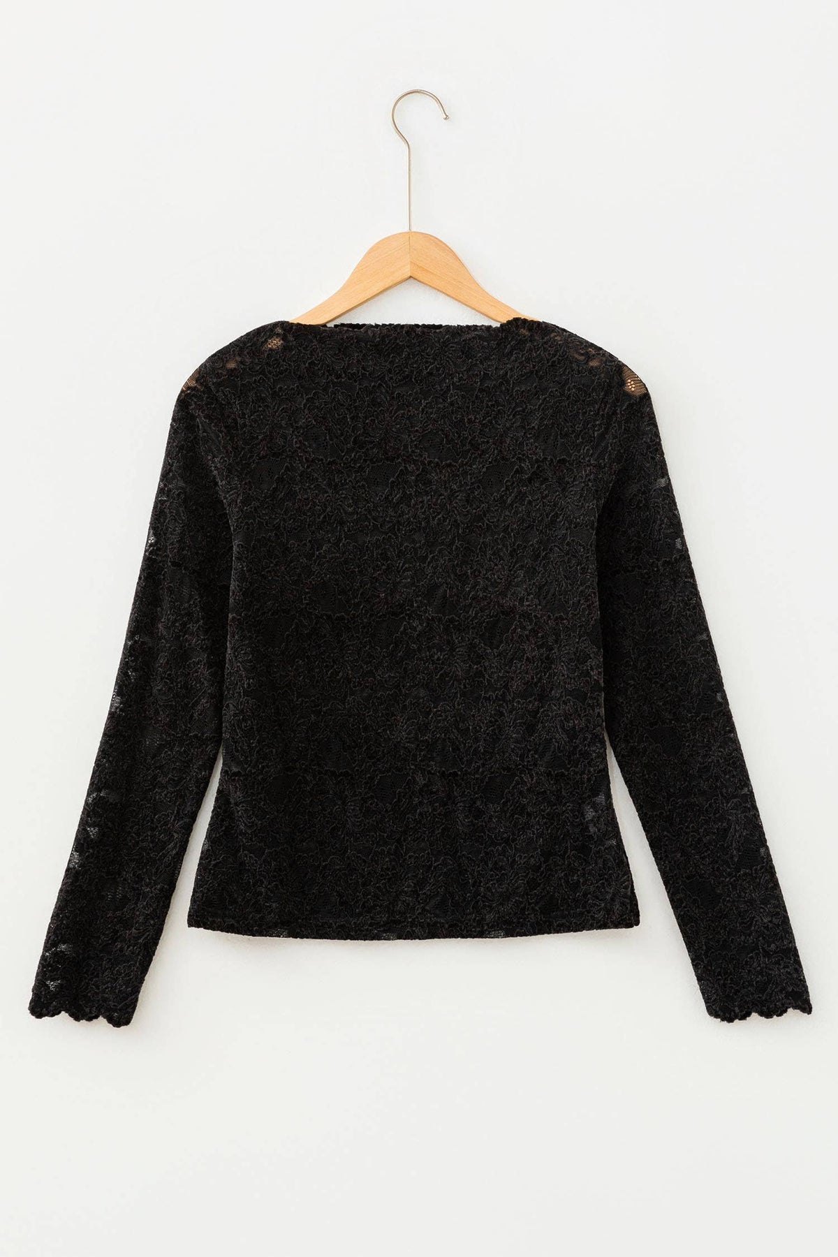 A black long-sleeve lace top with scalloped edges and sheer shoulder details, hanging on a wooden hanger against a plain white background.