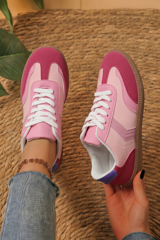 Pink sneakers with white laces worn on a textured surface