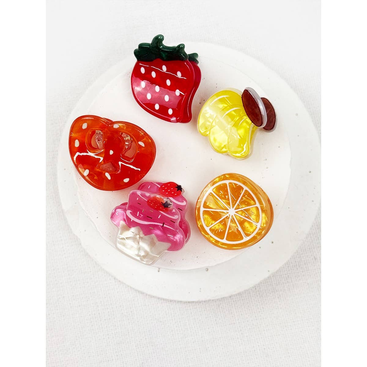 Colorful fruit-shaped hair clips on a white plate