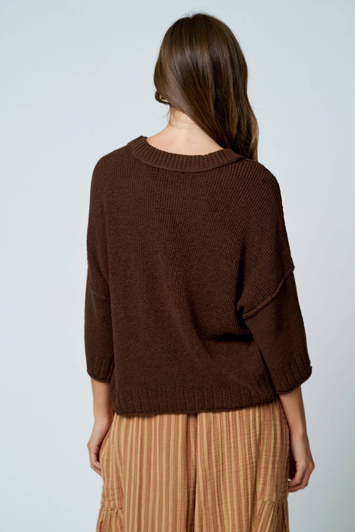 Person wearing a brown sweater and beige pants on a light gray background