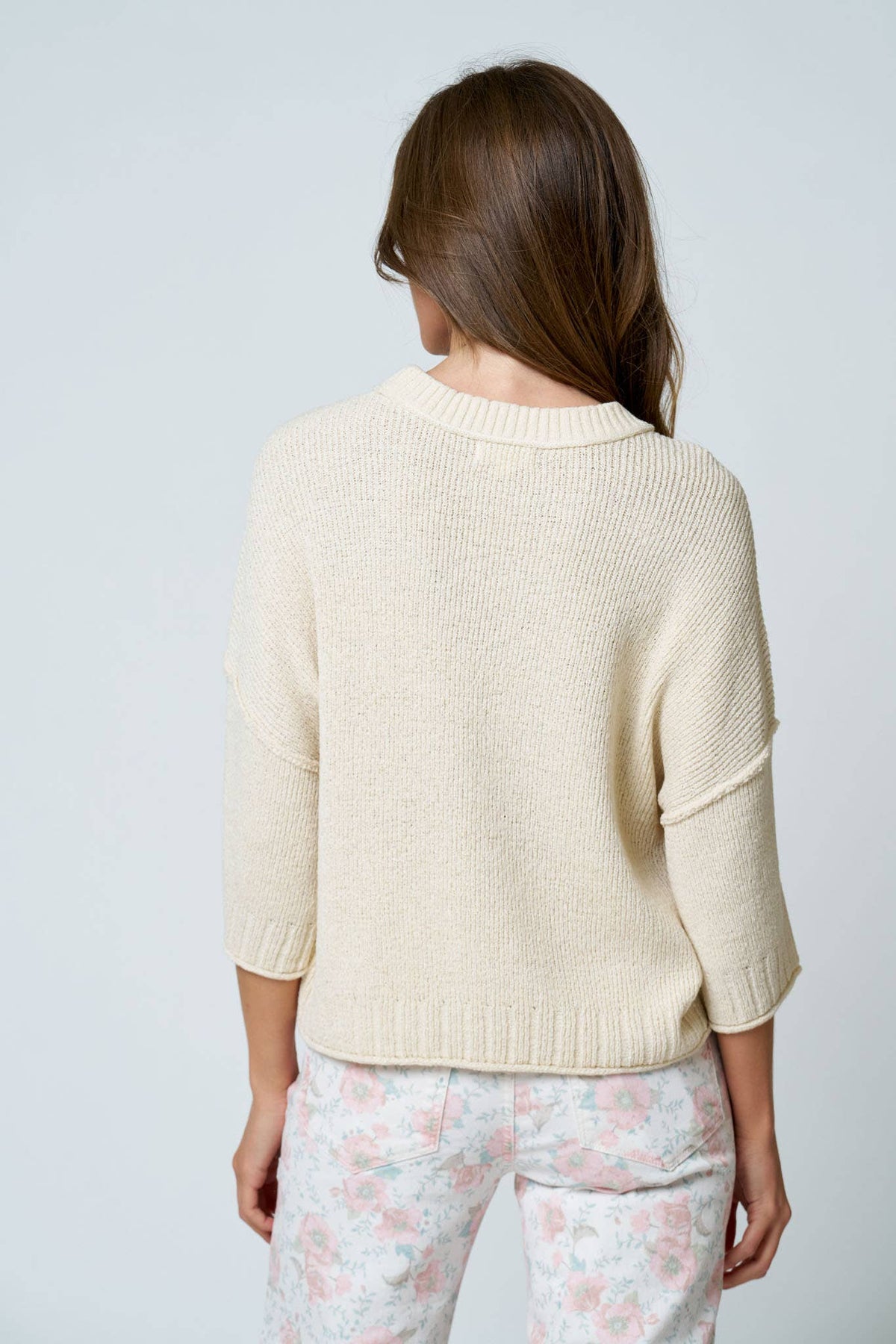 Woman wearing a cream sweater and floral pants against a light gray background