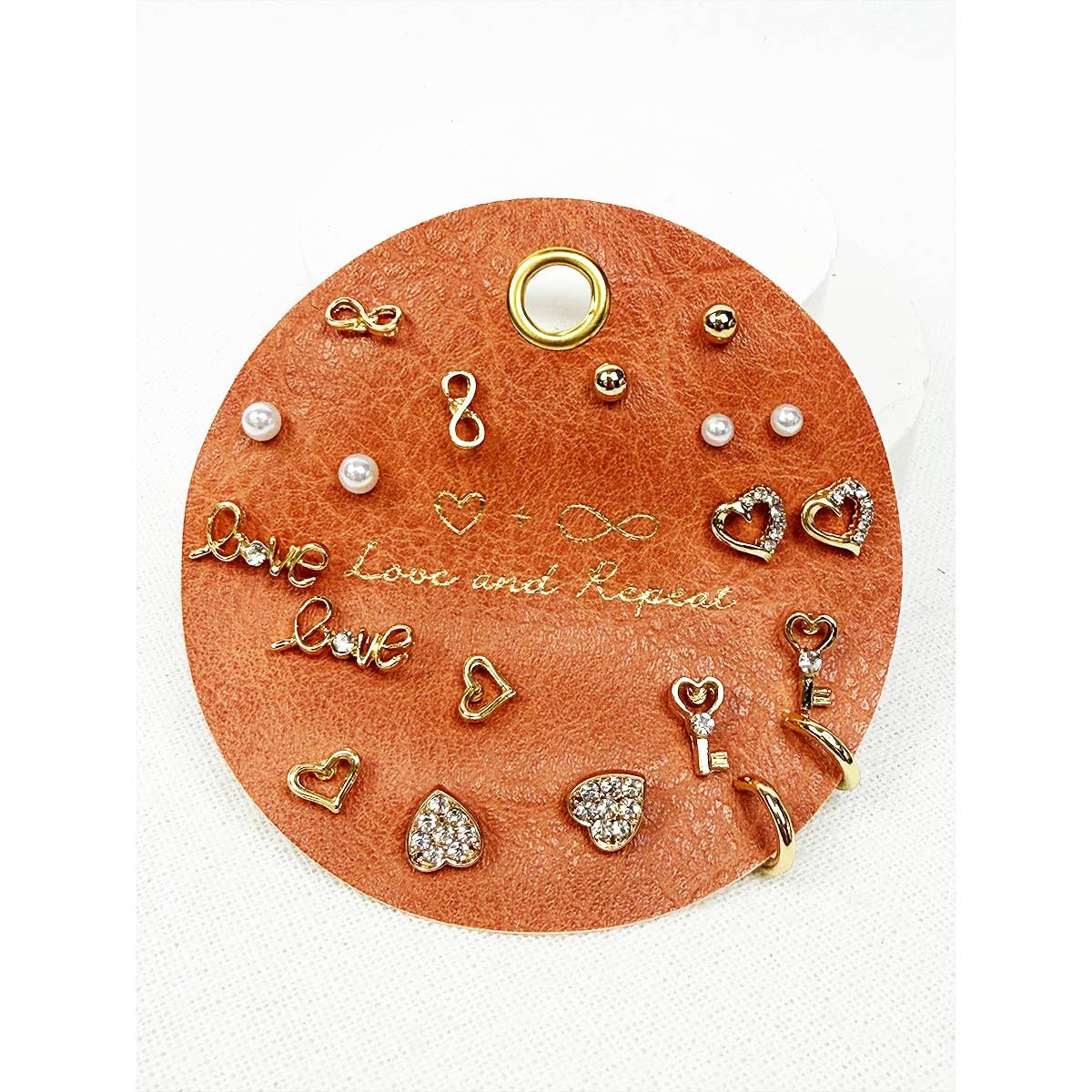 Collection of gold and pearl earrings on a round leather card with 'Love' and 'Repeat' text.
