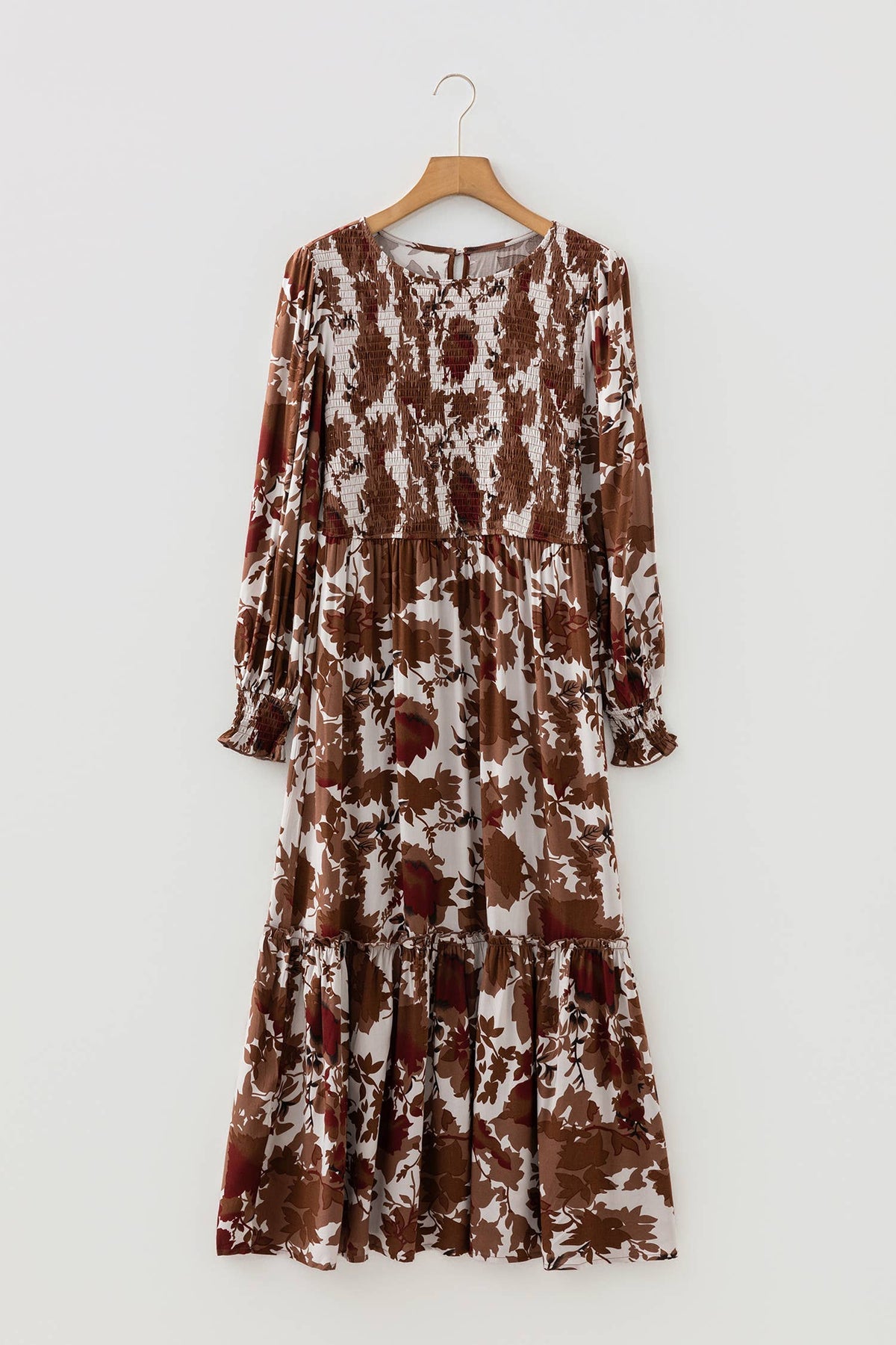A long-sleeve tiered maxi dress with a brown and white abstract floral pattern, hanging on a wooden hanger against a light gray background.