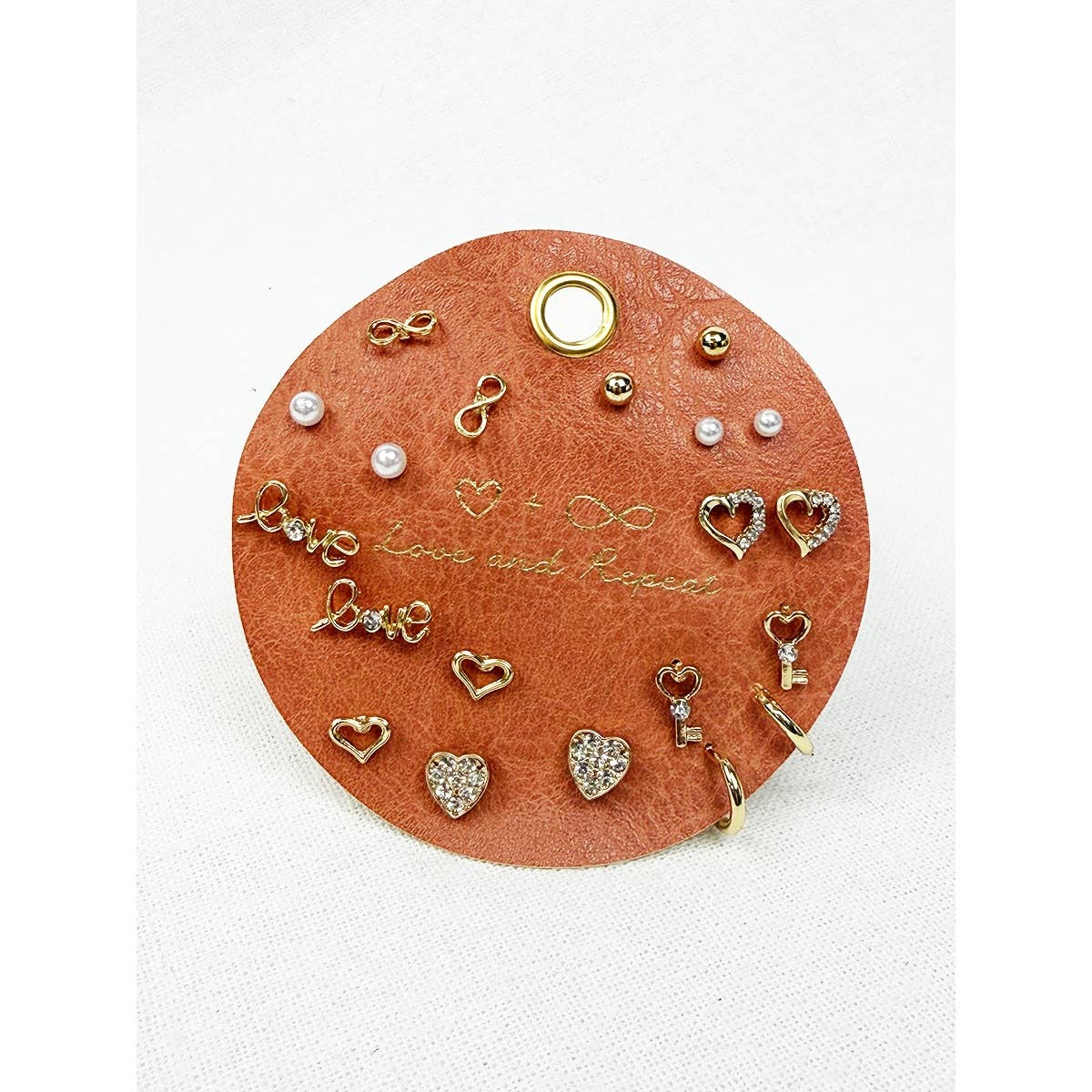 Collection of gold and rose gold earrings on a round, brown leather holder with 'love' engraved.