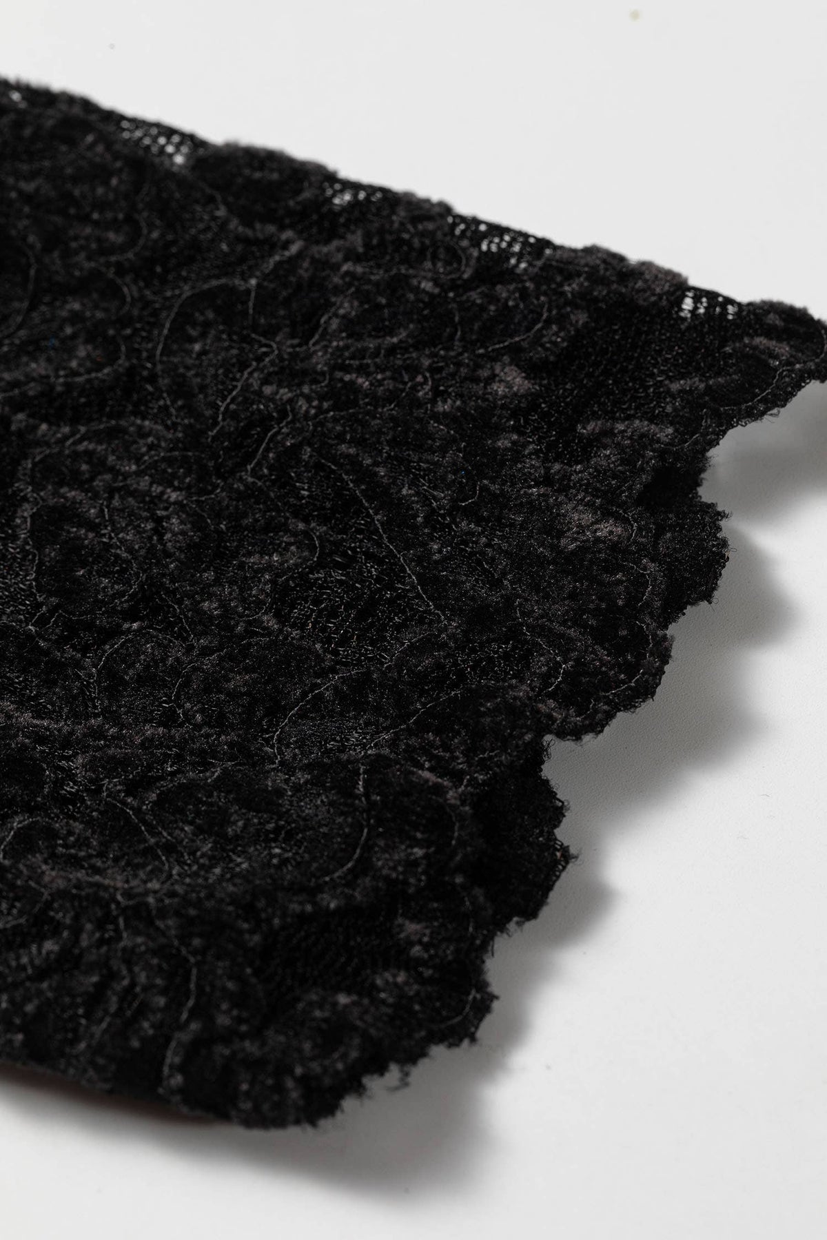 A close-up of black lace fabric with a textured, floral pattern and ruffled edge, shown on a plain white background.