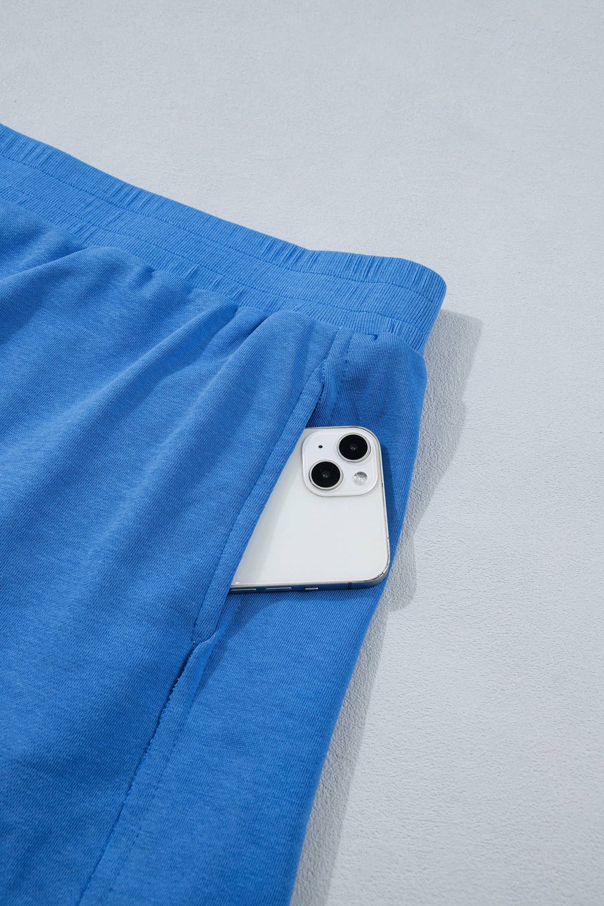 Blue skort with a smartphone peeking out from a pocket on a light gray background