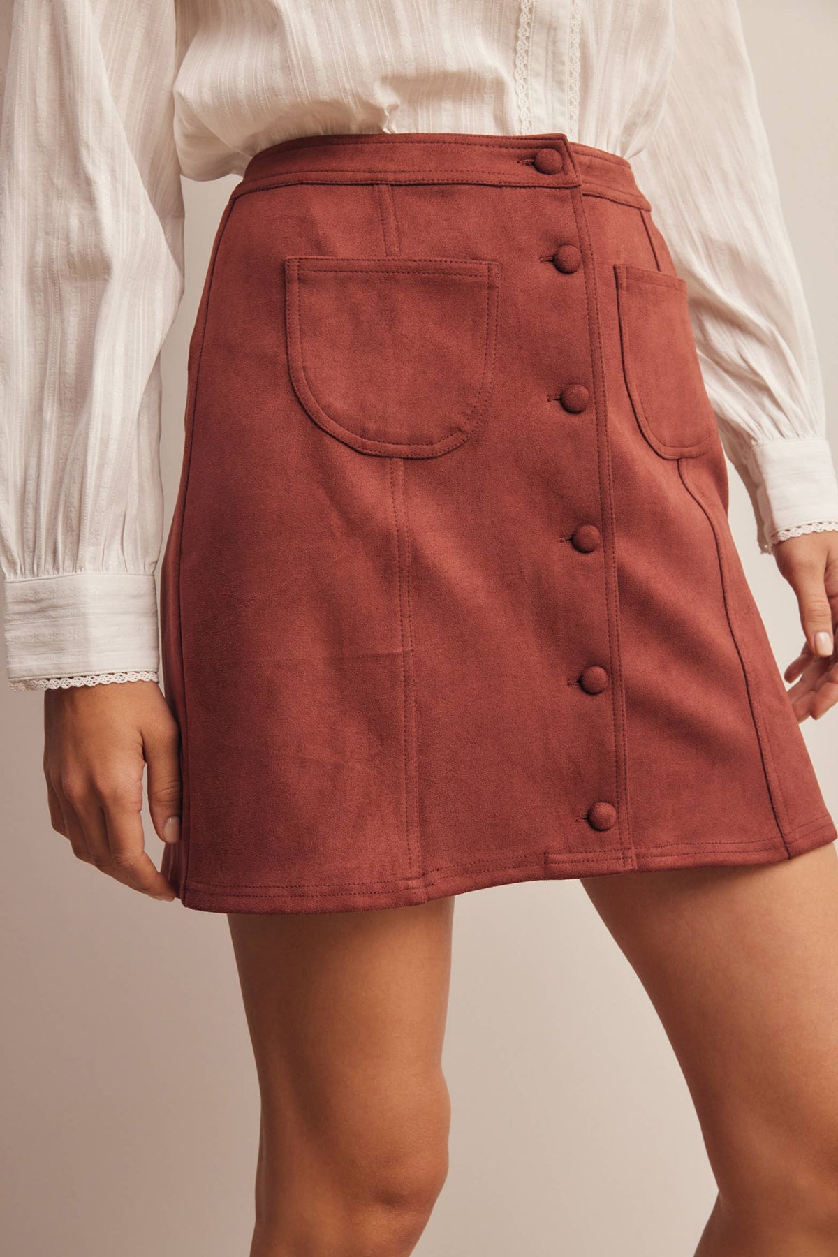 Person wearing a rust-colored skirt with button details on a neutral background