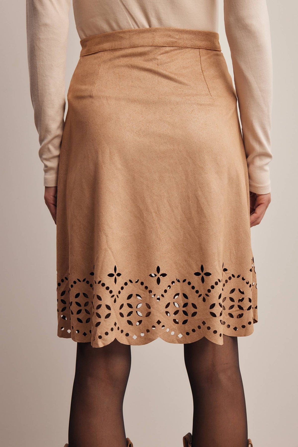A tan knee-length skirt with a scalloped eyelet lace hem, worn by a model with a cream long-sleeve top and sheer black tights.