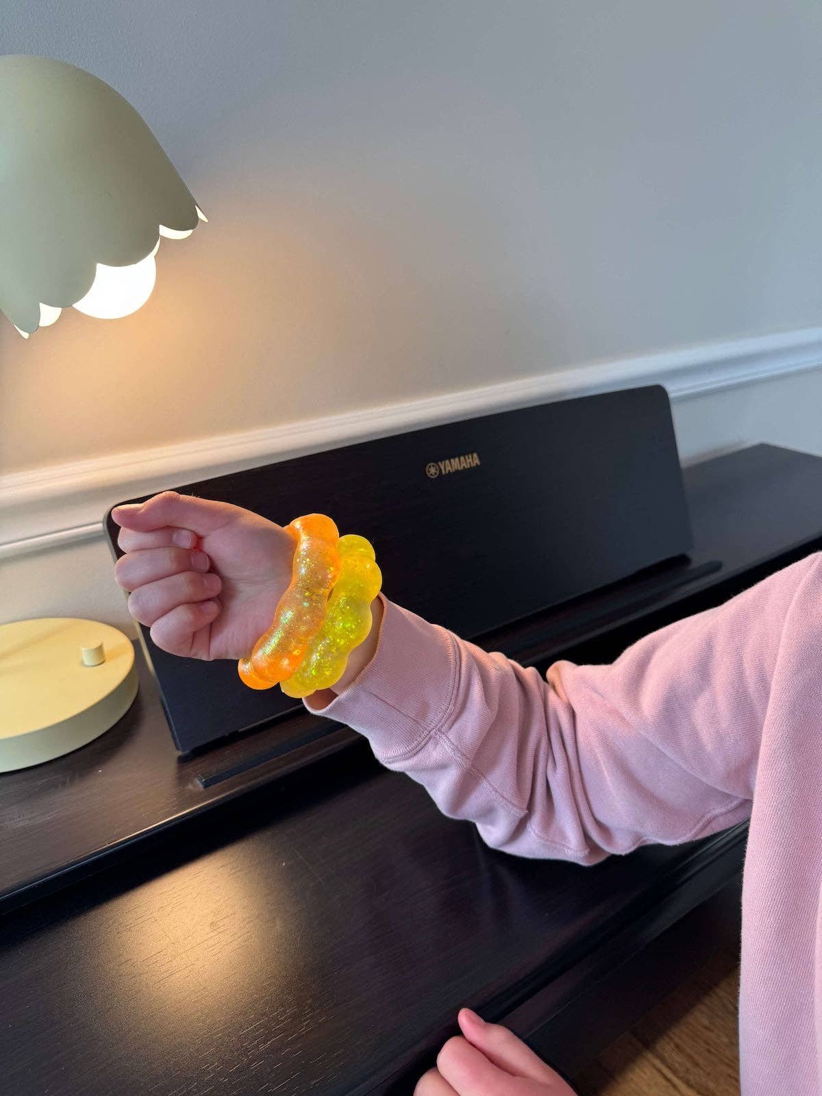Person wearing a yellow and an orange squish bracelet on a piano.