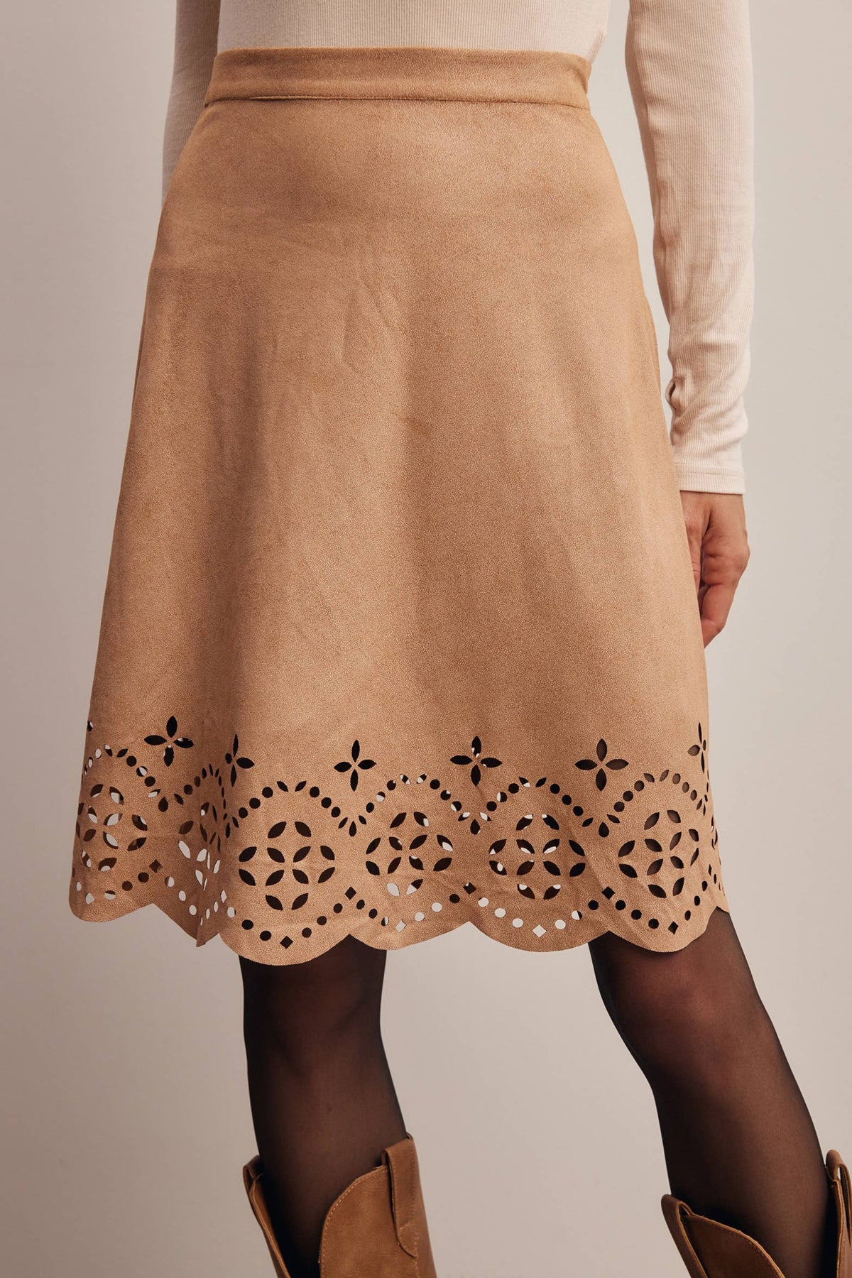 A tan suede-like A-line skirt with a scalloped eyelet lace hem, worn with a cream long-sleeve top and dark tights.