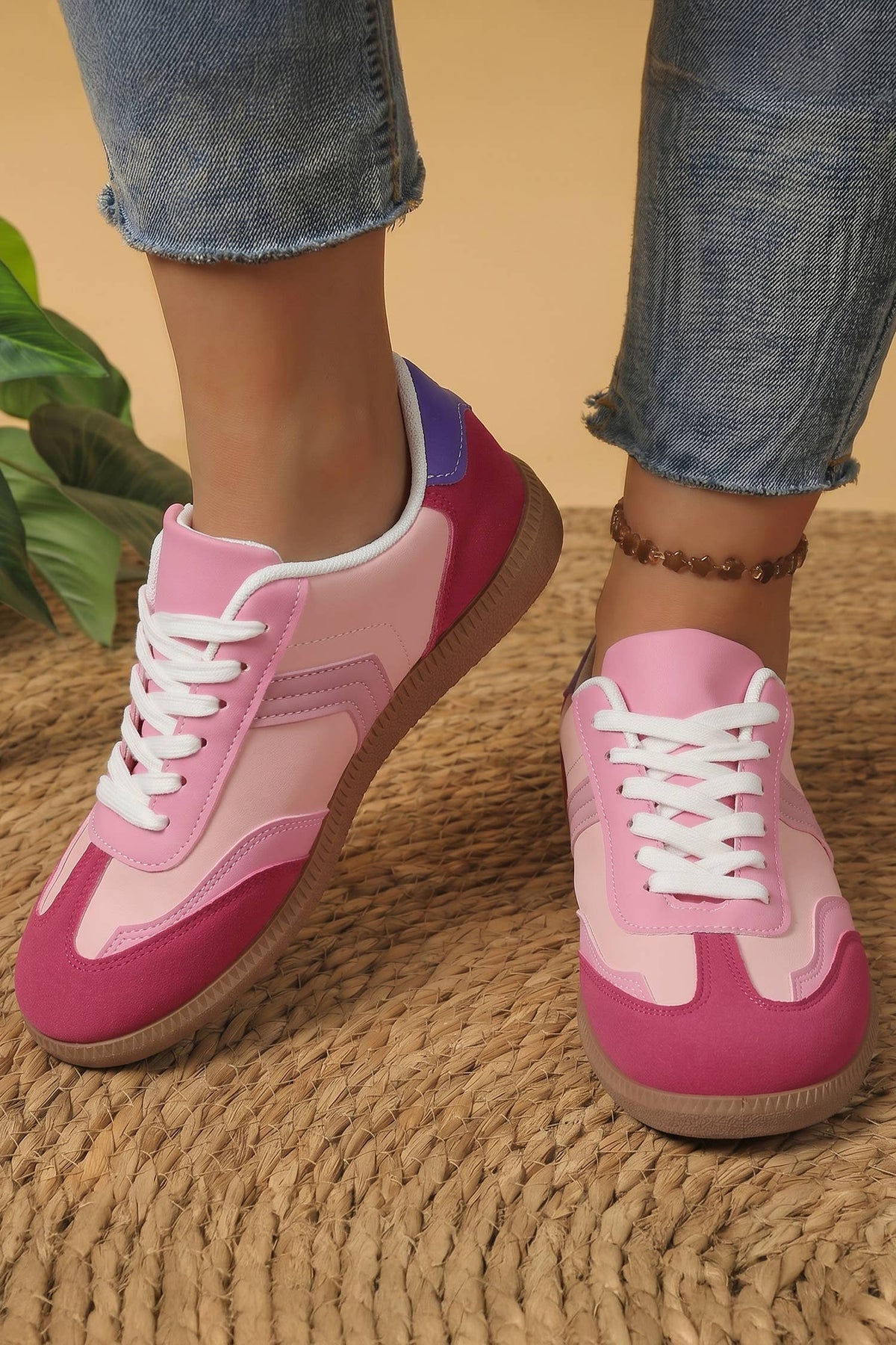 Pink and purple sneakers worn with blue jeans on a textured surface.