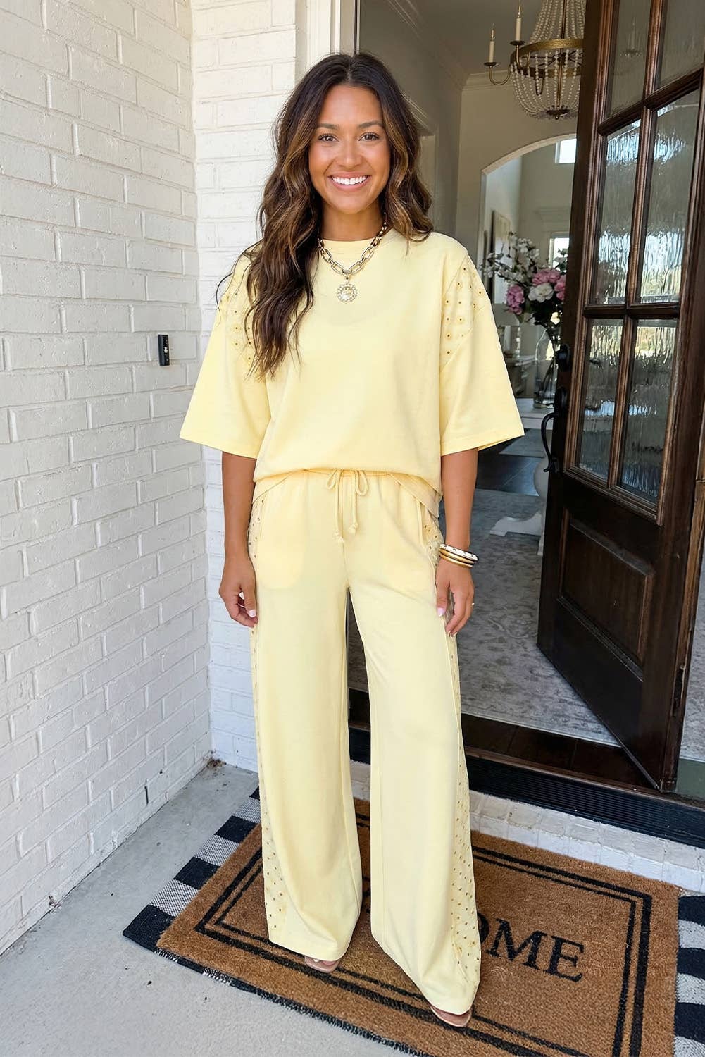 Woman in a yellow outfit standing in front of a door with a 'WELCOME' mat.